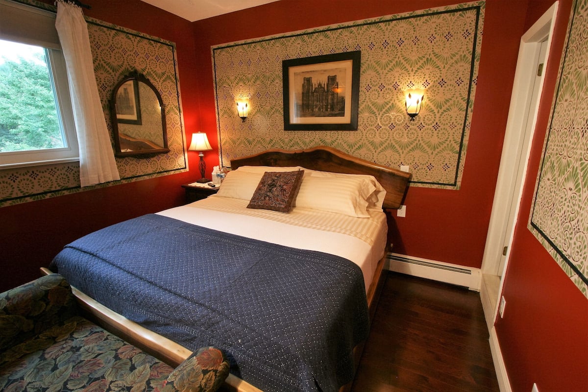Un dormitorio con cama, mesita de noche, lámpara, ventana con cortina y papel tapiz estampado.