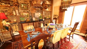 A dining room with a wooden table set for six, surrounded by chairs, with a stone wall and various decorative items. - Alpenhof Bed and Breakfast (Media)