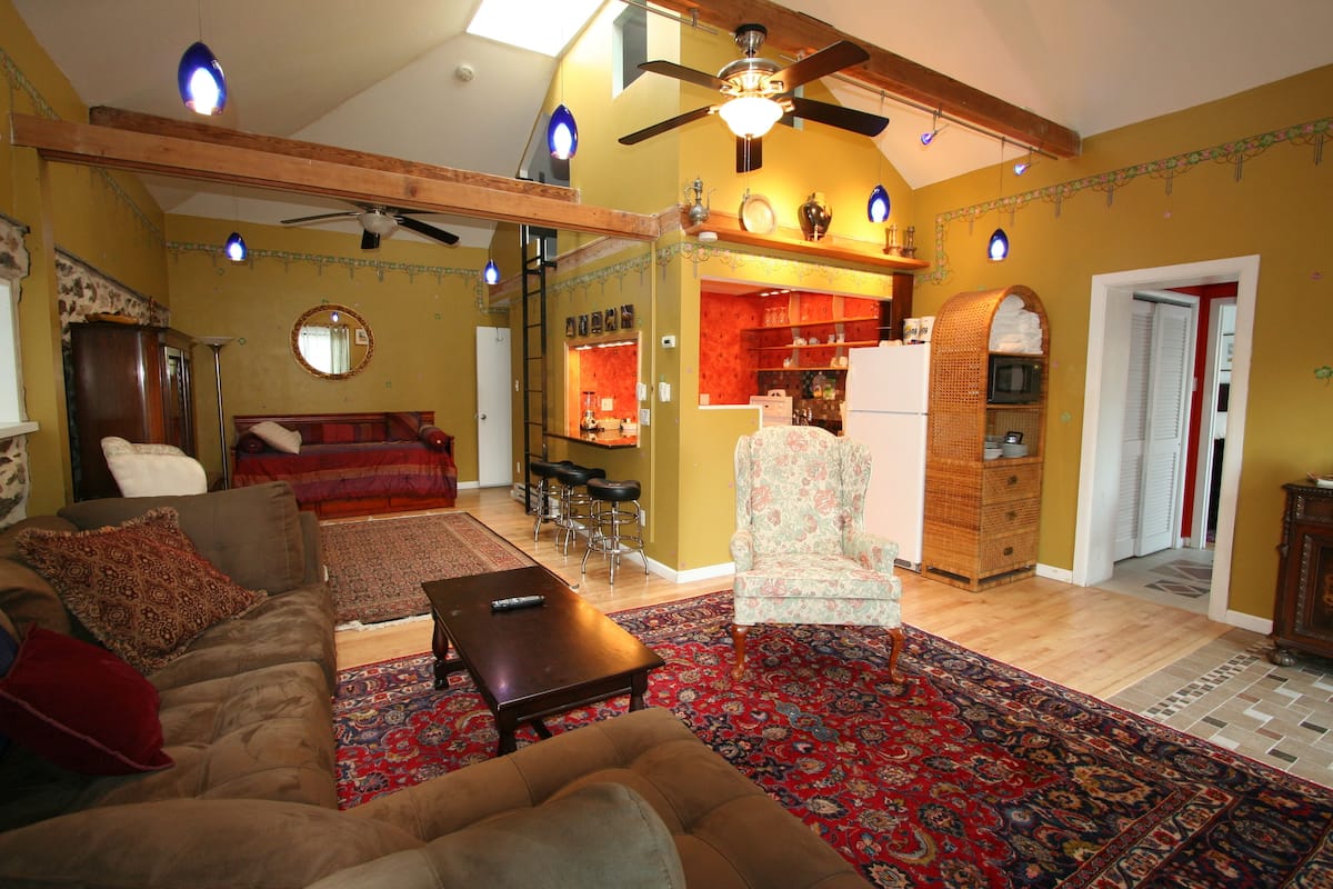 Una sala de estar con sofá, sillón y mesa de centro, un comedor con sillas y una cocina con refrigerador y microondas.