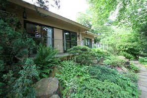 A house with a covered porch, surrounded by lush greenery and large rocks. - Alpenhof Bed and Breakfast (Media)