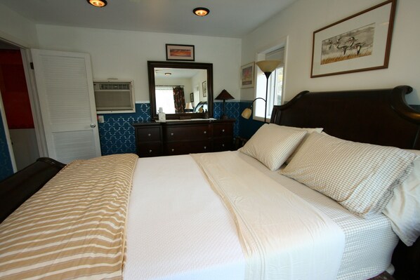 A neatly made bed with a striped bedspread, a dresser with a mirror above it, and a framed picture on the wall.