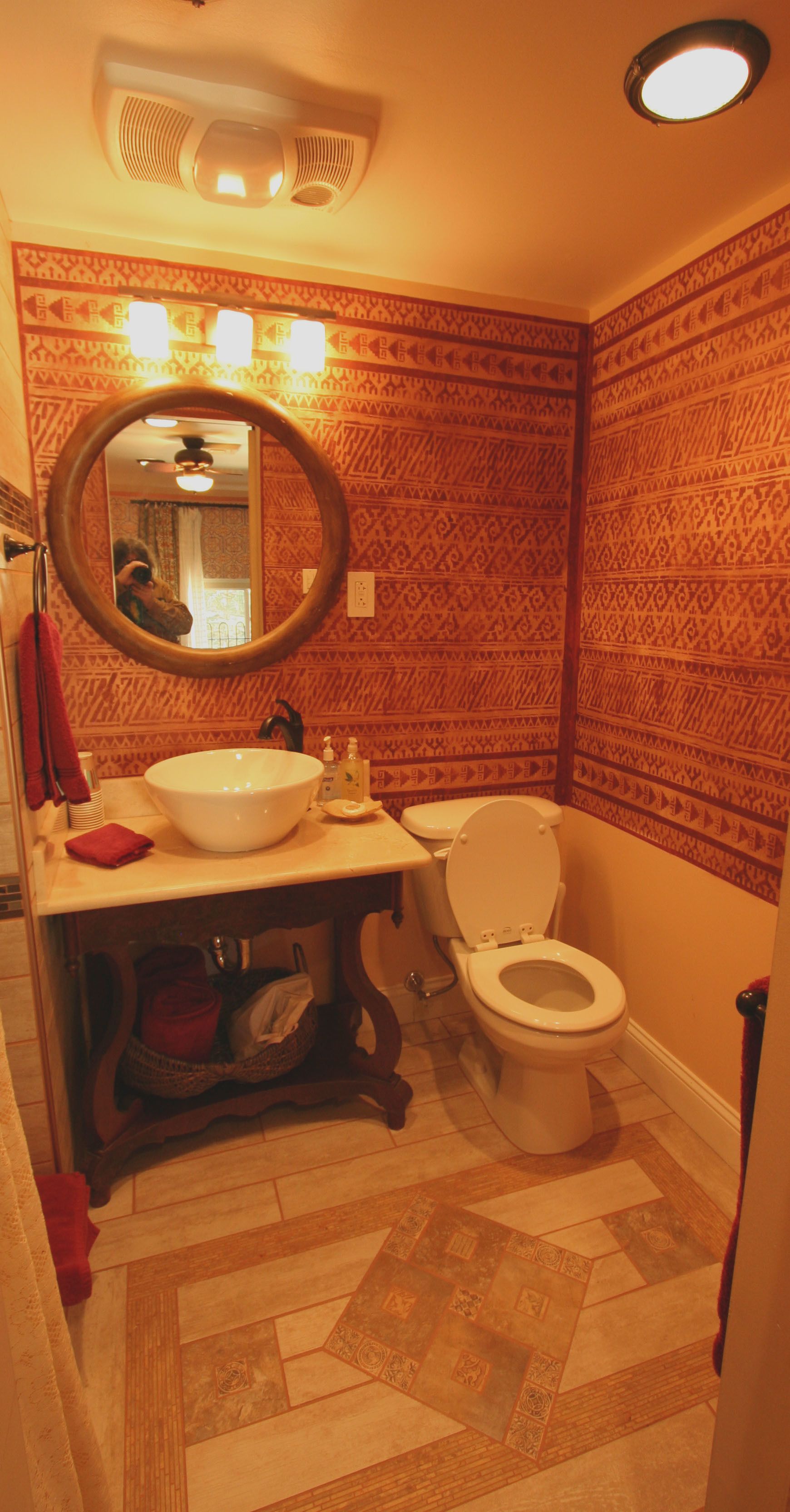 Une salle de bain avec un papier peint à motifs, un miroir rond, un lavabo et des toilettes.