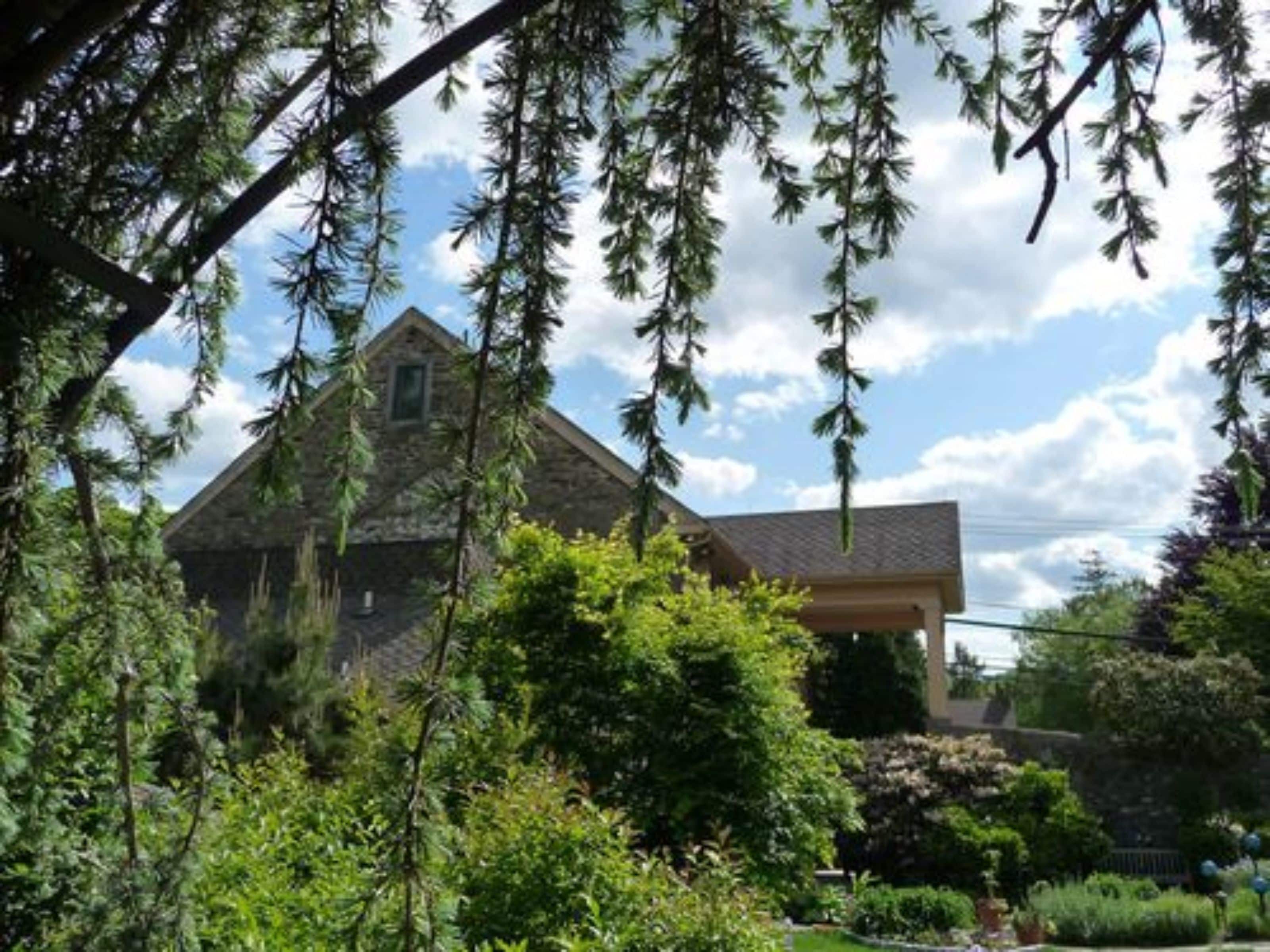A stone house with a gabled roof, surrounded by lush greenery and trees.
