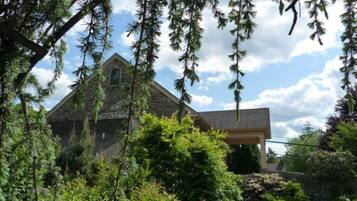A stone house with a gabled roof, surrounded by lush greenery and trees.