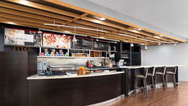 Un bar-bistro moderne avec un comptoir incurvé, des tabourets de bar et un tableau affichant le menu.