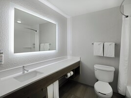 Un baño moderno con un espejo grande, lavabo blanco, tocador de madera, inodoro y perchero para toallas.