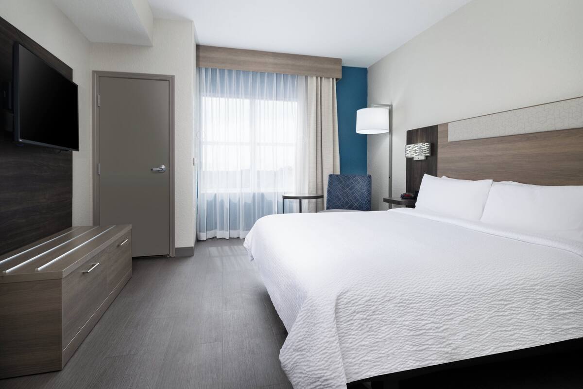 A hotel room with a large bed, a flat-screen TV, a desk, and a chair.