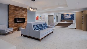 A modern lobby with a grey sofa, a flat-screen TV, wooden wall paneling, and a reception desk.