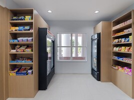 A narrow hallway with shelves stocked with snacks and beverages, a refrigerator, and a window with a view of the outdoors.