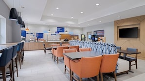 A modern hotel dining area with multiple seating options, including booths and tables, and a visible kitchen area in the background. - Holiday Inn Express & Suites Lakeland North - I-4 by IHG (Lakeland)