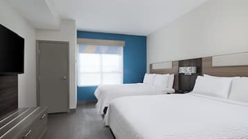 A hotel room with two beds, a TV, a wooden headboard, and a window with blinds.