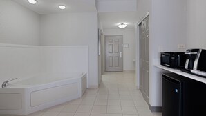 A modern bathroom with a bathtub, a toilet, and a sink. There is a microwave and a coffee maker on a counter.