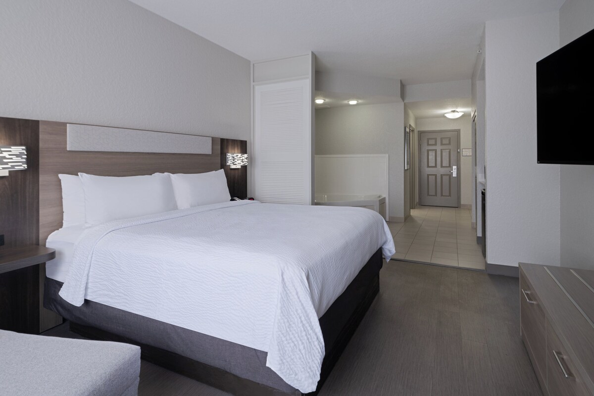 Habitación de hotel moderna con una cama grande, mesitas de noche, un televisor de pantalla plana y un baño visible a través de una puerta abierta.