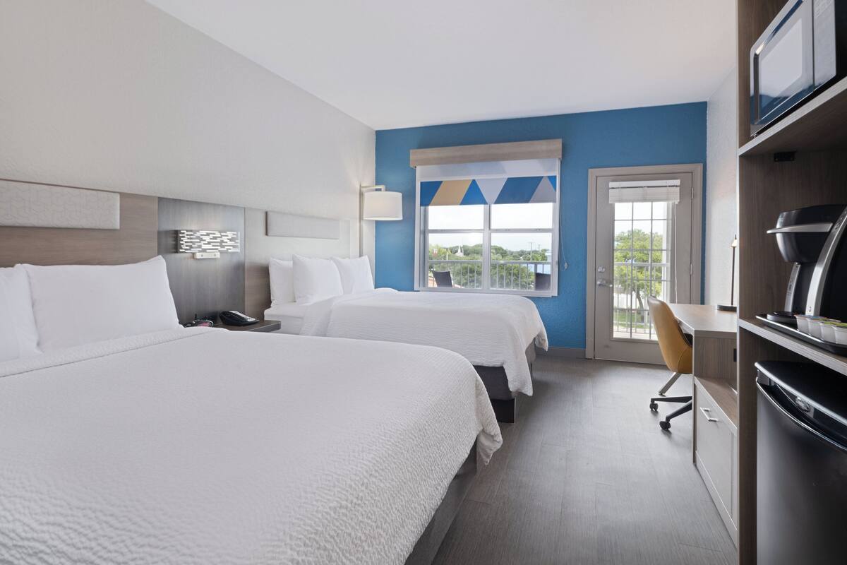 A hotel room with two beds, a desk, a chair, and a television.
