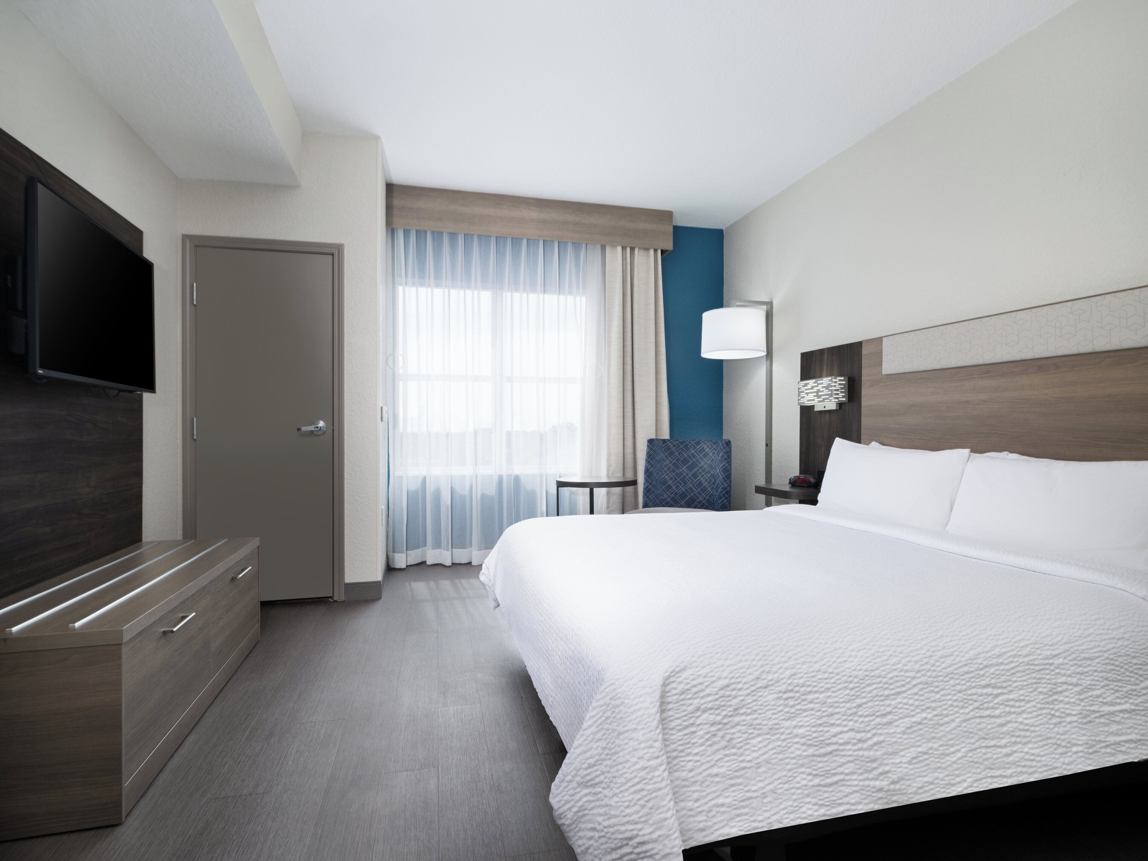 Una habitación de hotel con una cama grande, un televisor de pantalla plana, un escritorio y una silla.