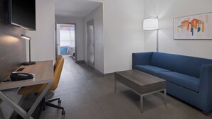 A modern hotel room with a desk, chair, sofa, and a flat-screen TV mounted on the wall.