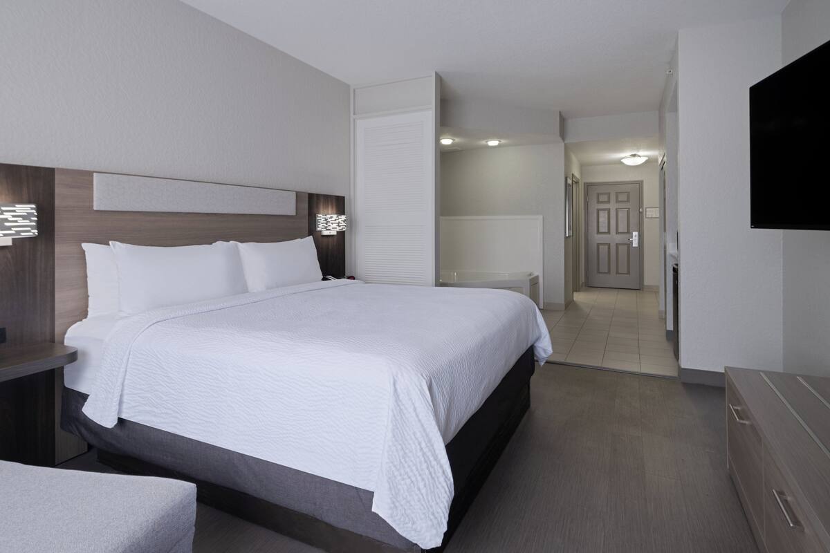 A modern hotel room with a large bed, bedside tables, a flat-screen TV, and a bathroom visible through an open door.