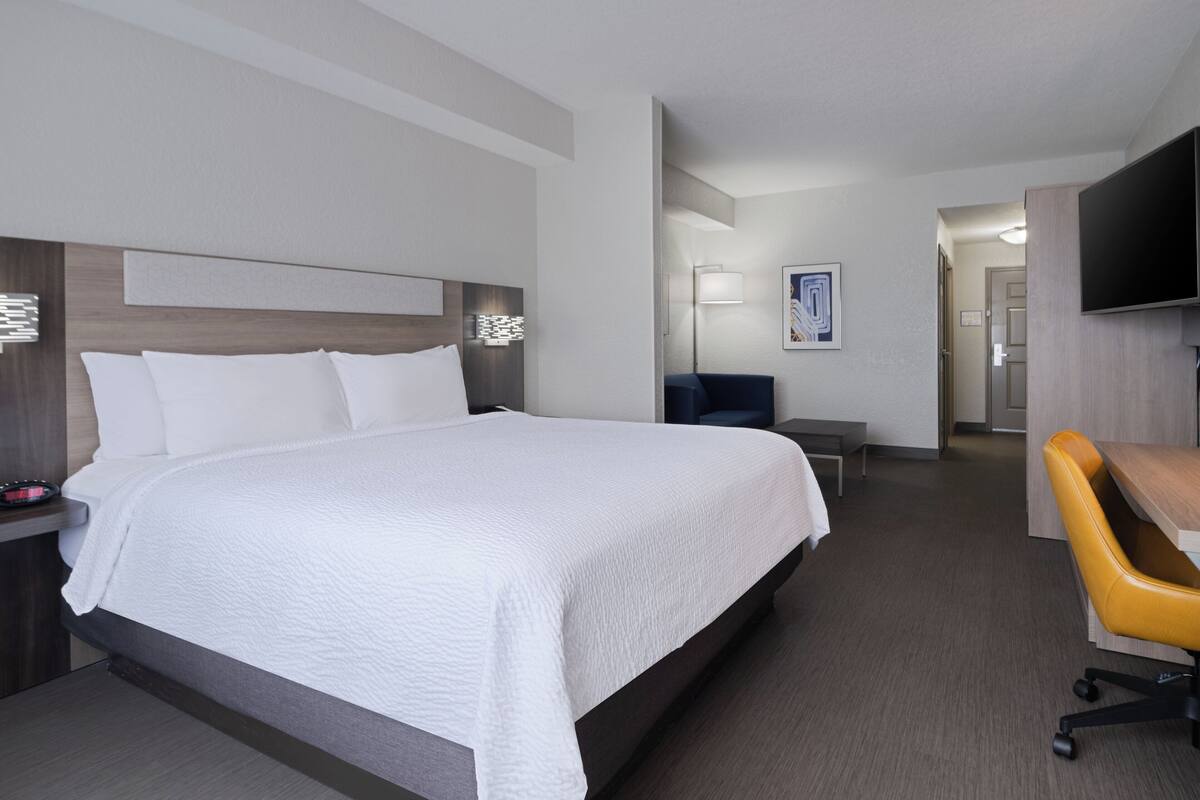 A hotel room with a large bed, a desk, a chair, and a television.