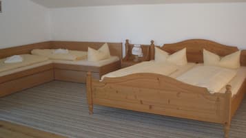 A room with two wooden beds, each with a wooden headboard and a bedside table. The room has a carpeted floor and plain white walls.