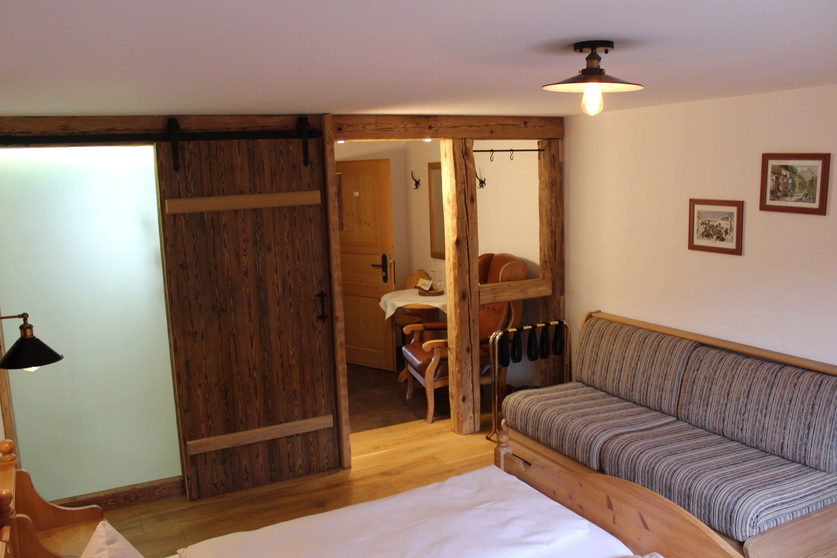 Una habitación acogedora con una cama de madera, un sofá a rayas y una puerta de madera que da a un comedor.