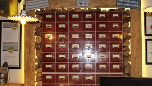 Un mur composé de boîtes de rangement en métal rouge, chacune portant une étiquette, une étagère en bois sur laquelle sont empilés des bûches, et un panneau placé au-dessus des boîtes.
