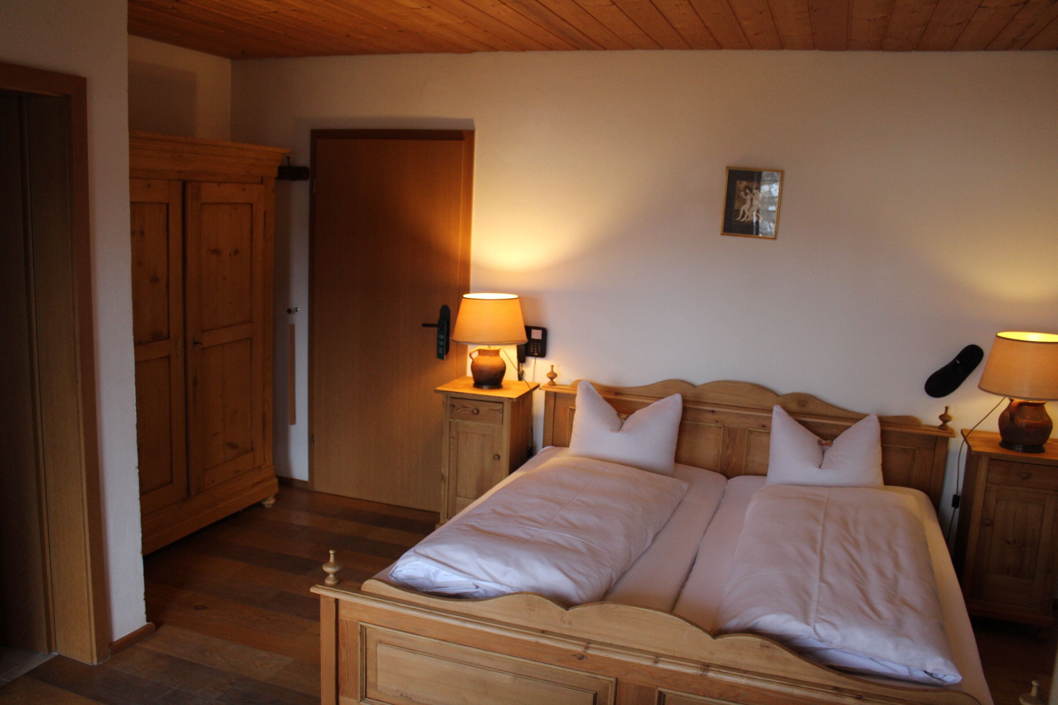 Ein Schlafzimmer mit einem hölzernen Bett, zwei Nachttischen mit Lampen, einem Holzschrank und einer Tür zu einem anderen Raum.
