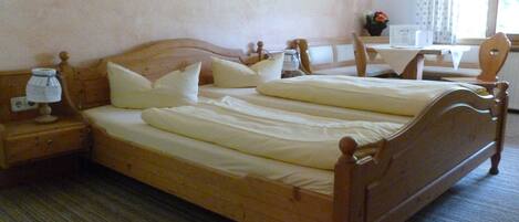 Una cama doble con cabecera y piecera de madera, una mesita de noche con lámpara y una ventana con cortinas.