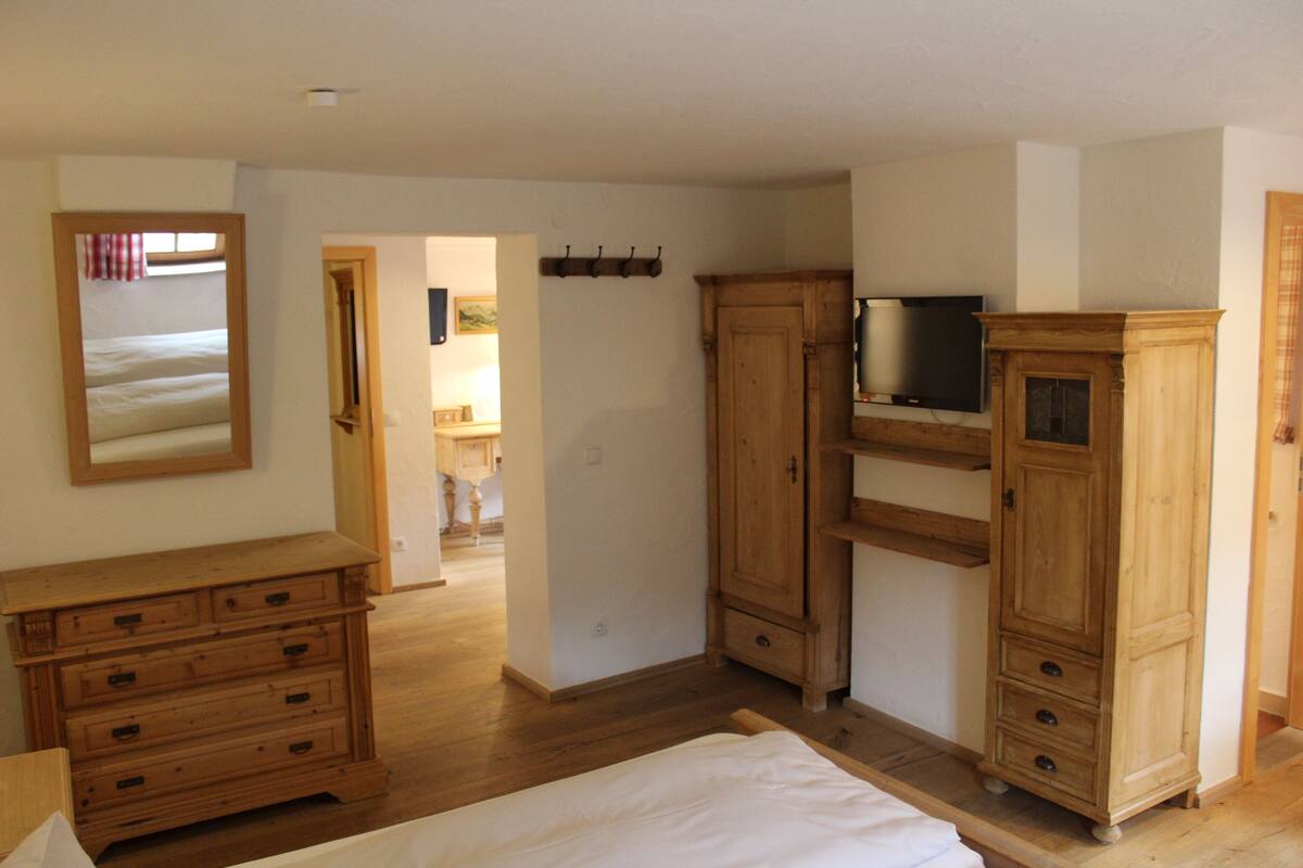 Une chambre à coucher avec une commode en bois, un lit et un téléviseur posé sur un meuble.