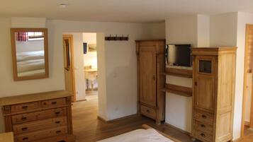 A bedroom with a wooden dresser, a bed, and a television on a stand.