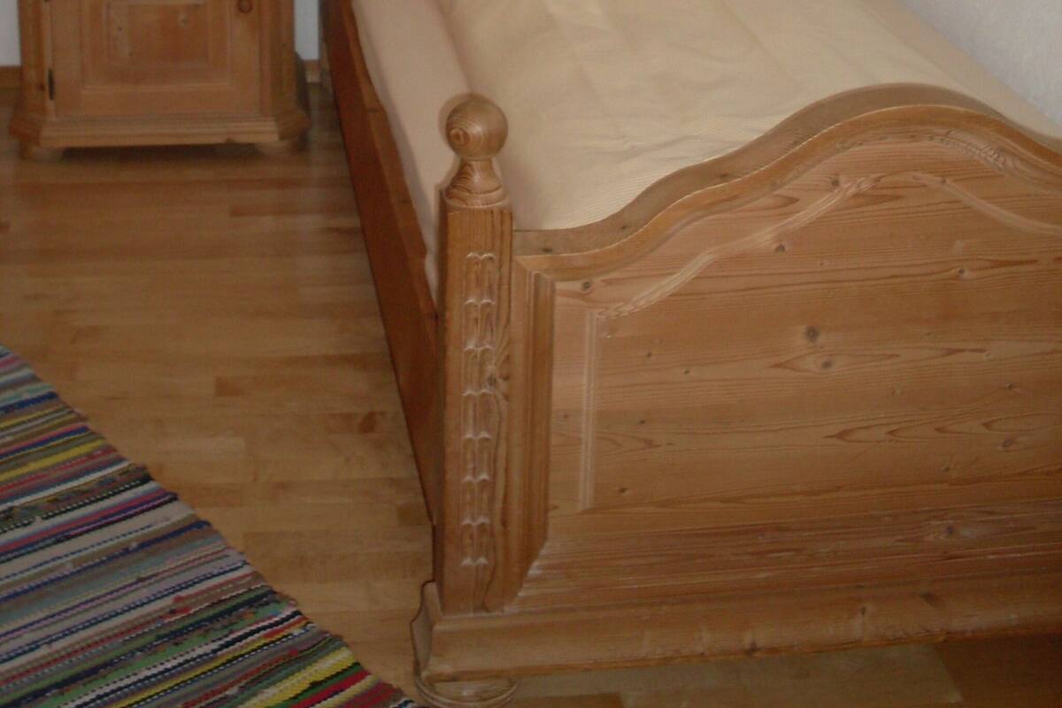 Un lit en bois avec une tête de lit, une table de chevet avec une lampe et une petite armoire.