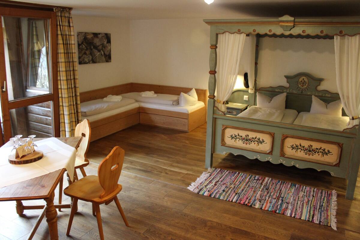 Une chambre à coucher avec un lit à baldaquin, une table en bois avec des chaises, un banc et une fenêtre avec des rideaux.
