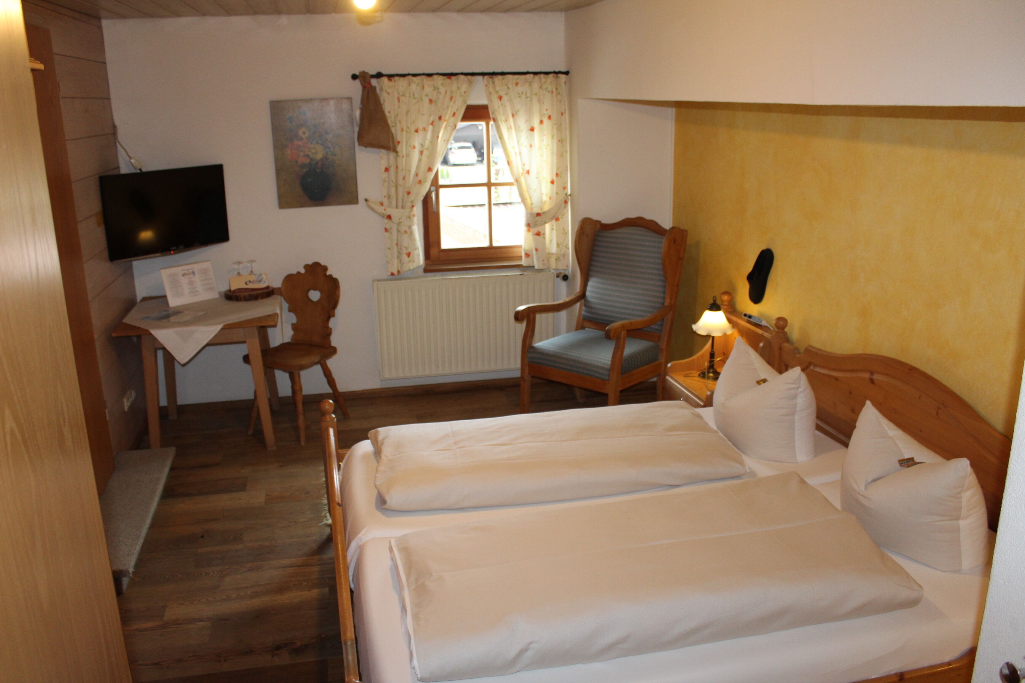 Ett hotellrum med två sängar, ett skrivbord med en stol, en tv och ett fönster med gardiner.