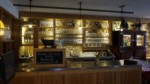 Un espace bar avec des étagères remplies de verres et de bouteilles, un panneau noir et un comptoir en bois.