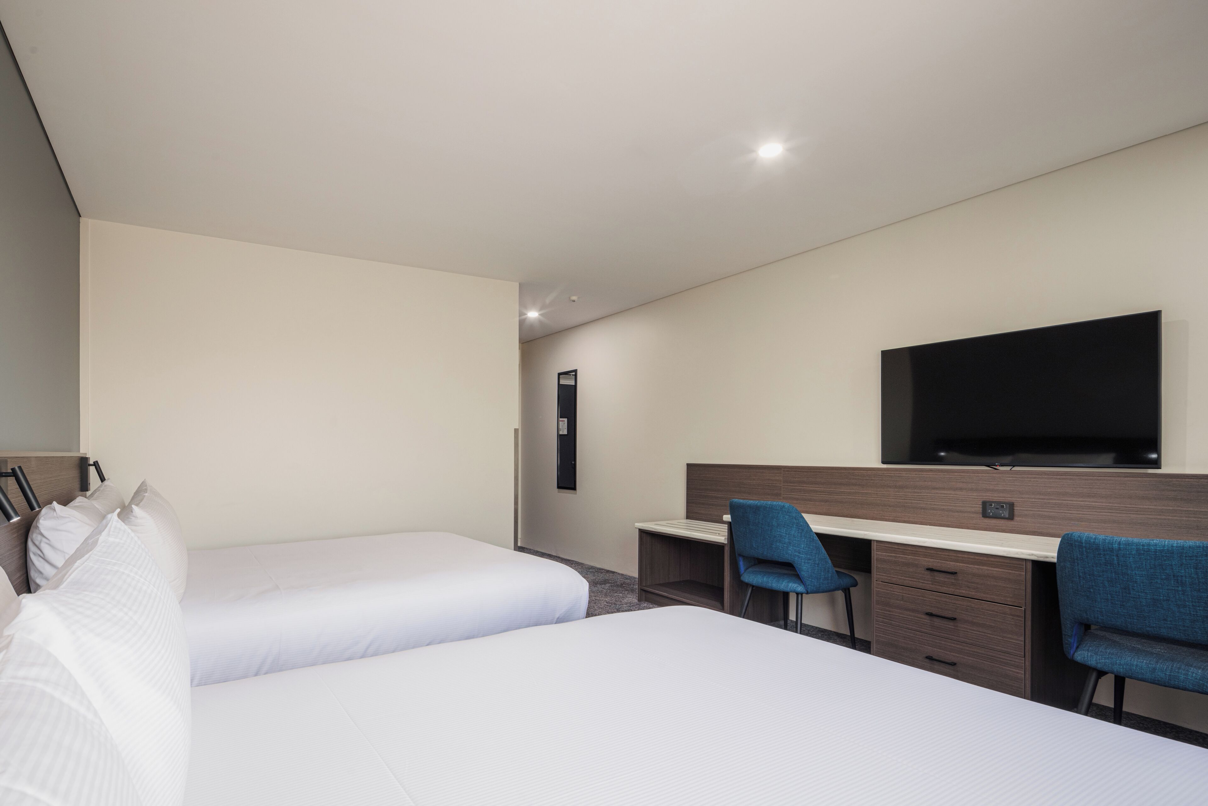 A hotel room with two beds, a desk, a chair, and a flat-screen TV.