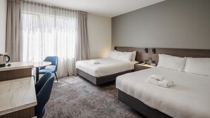 Habitación de hotel con dos camas, un escritorio, una silla y un ventanal con cortinas.