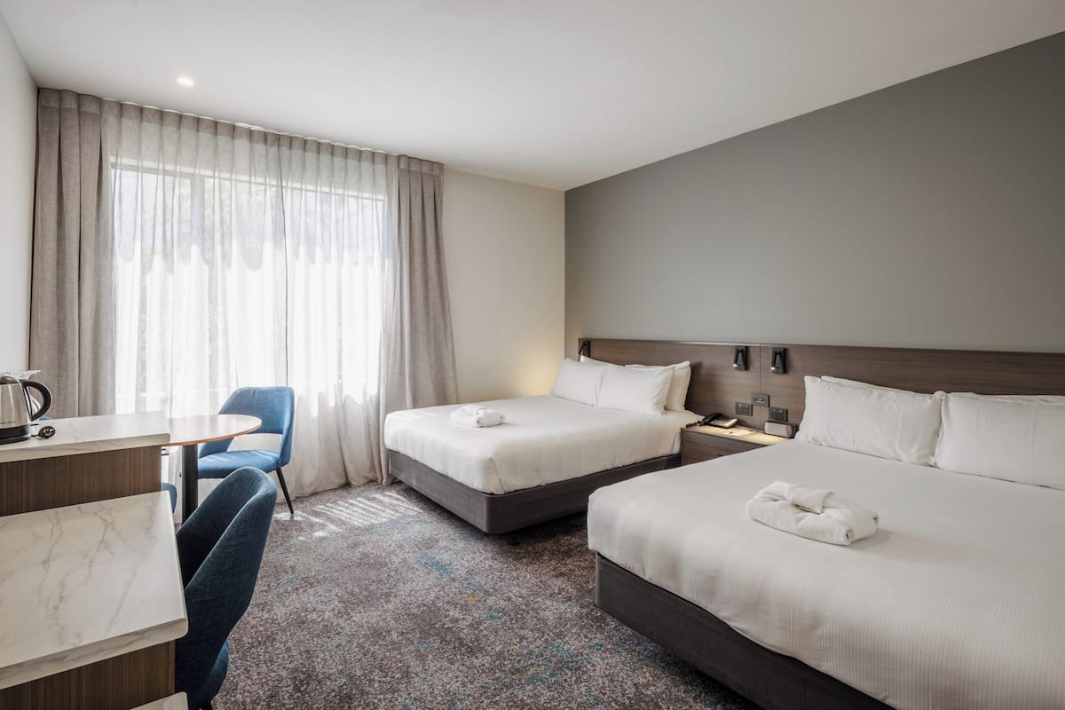Een hotelkamer met twee bedden, een bureau, een stoel en een groot raam met gordijnen.