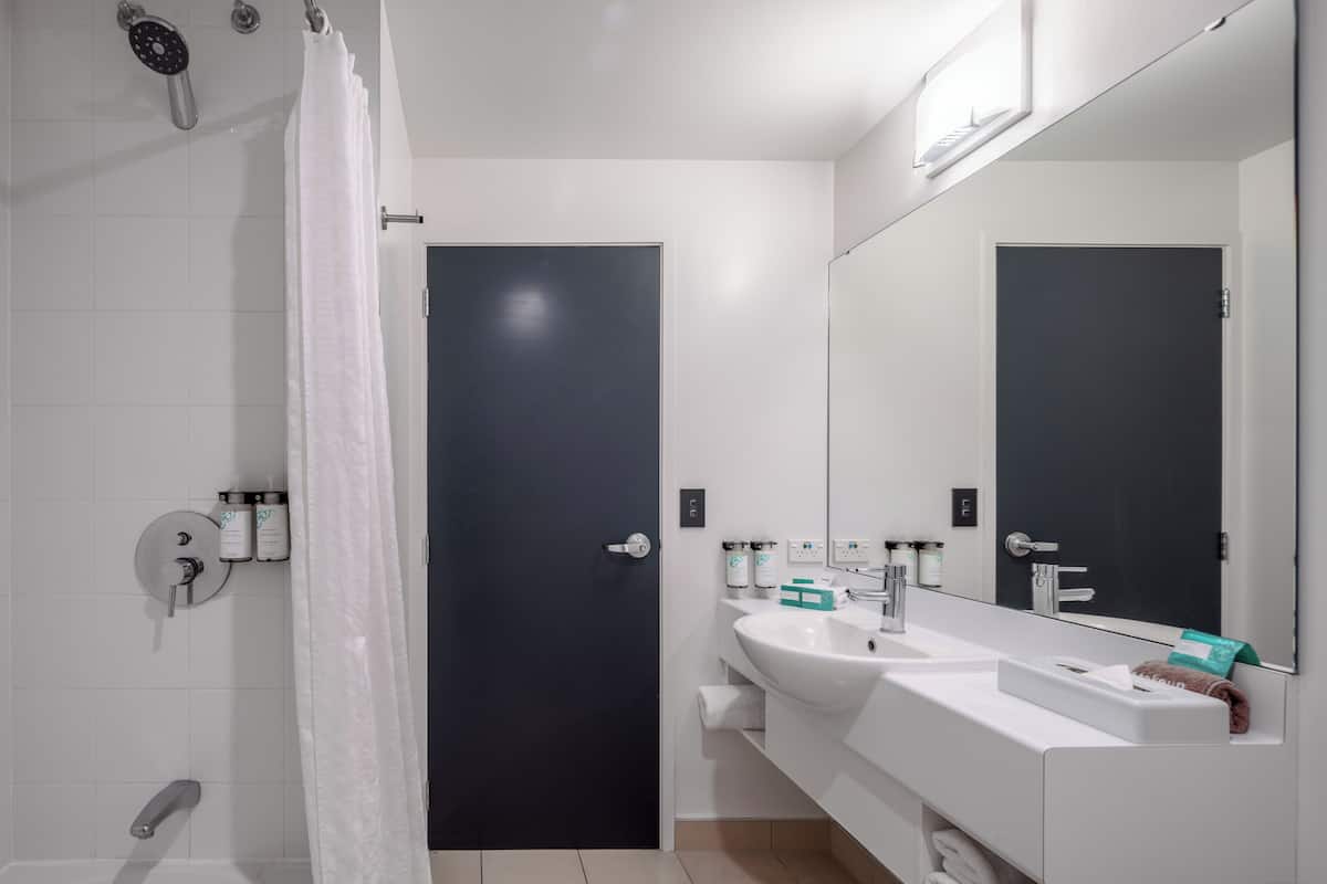 Een moderne badkamer met een witte wastafel, een grote spiegel en een donkere deur.