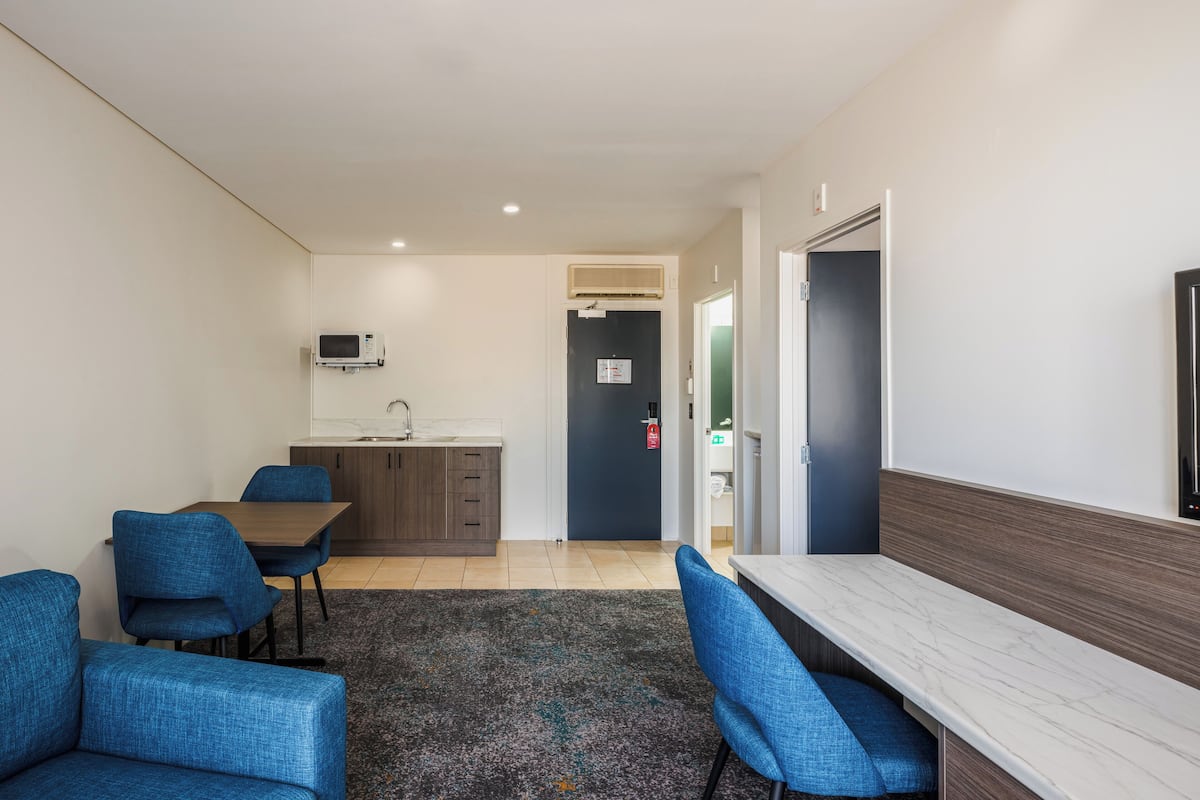 Een moderne hotelkamer met een zithoek, een kitchenette en een zithoek met blauwe fauteuils.