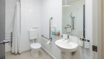 A bathroom with a toilet, sink, shower, and hand sanitizer dispensers.