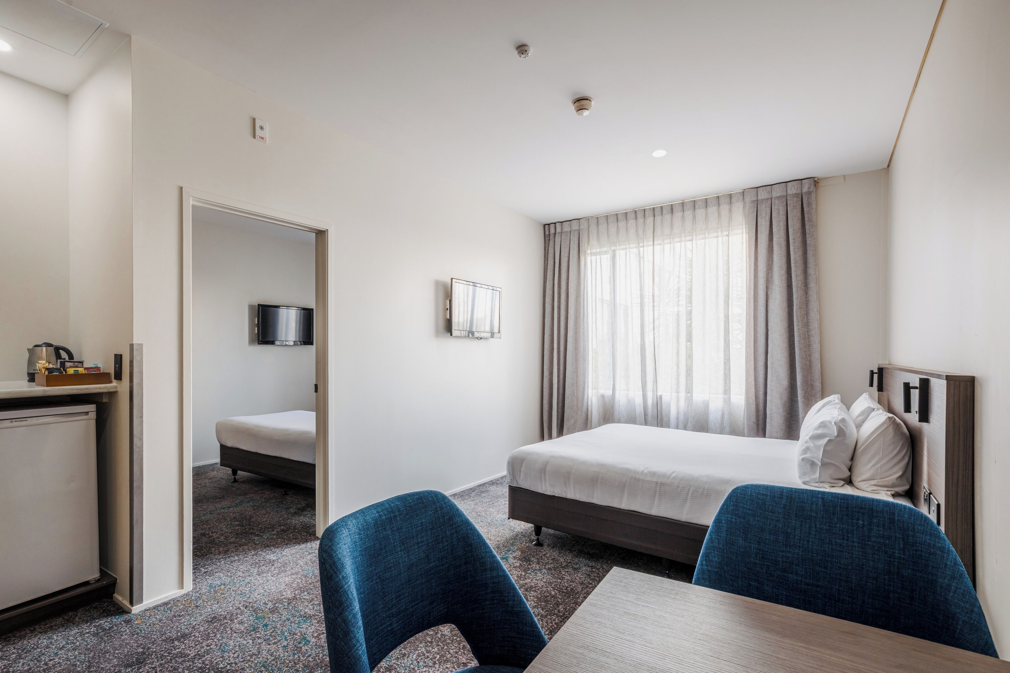 A hotel room with a bed, a desk, a chair, a TV, and a window with curtains.