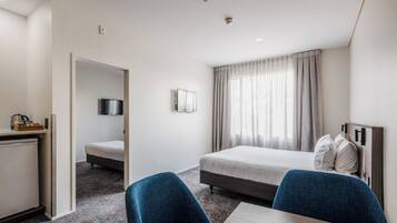 A hotel room with a bed, a desk, a chair, a TV, and a window with curtains.