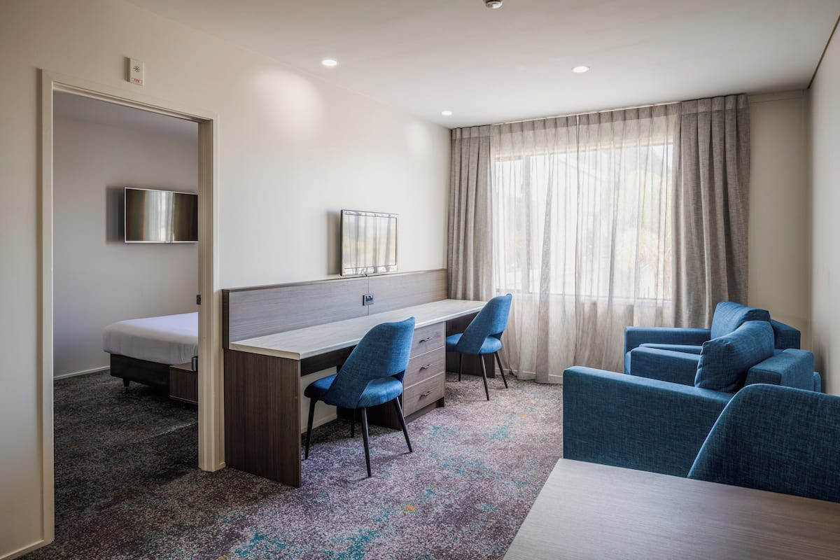 Een hotelkamer met een bed, een bureau met twee stoelen, een televisie en een groot raam met gordijnen.