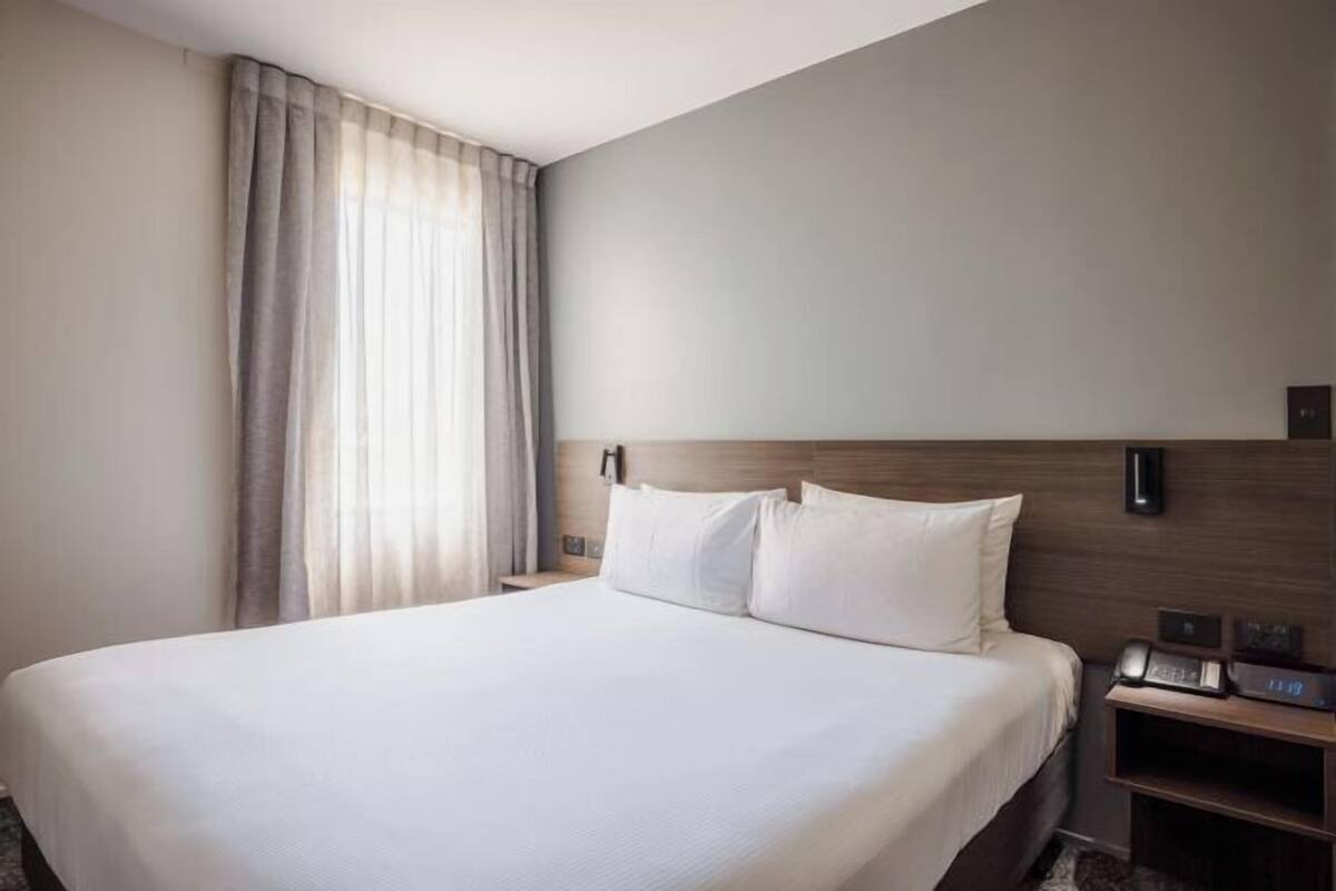 Een hotelkamer met een groot bed, een nachtkastje met een telefoon en een wandlamp.