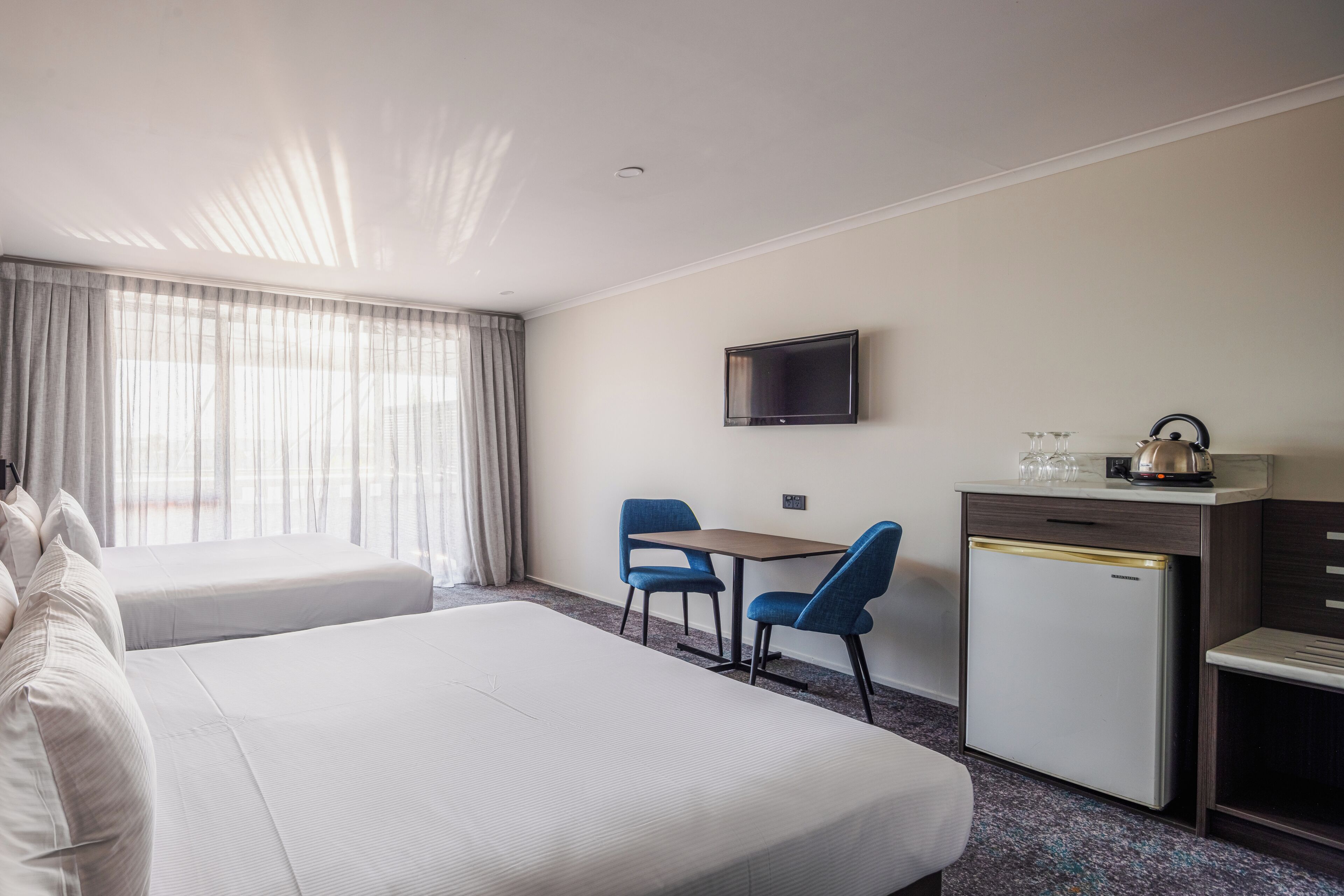 Habitación de hotel con dos camas, un escritorio con sillas, televisión y un minibar.