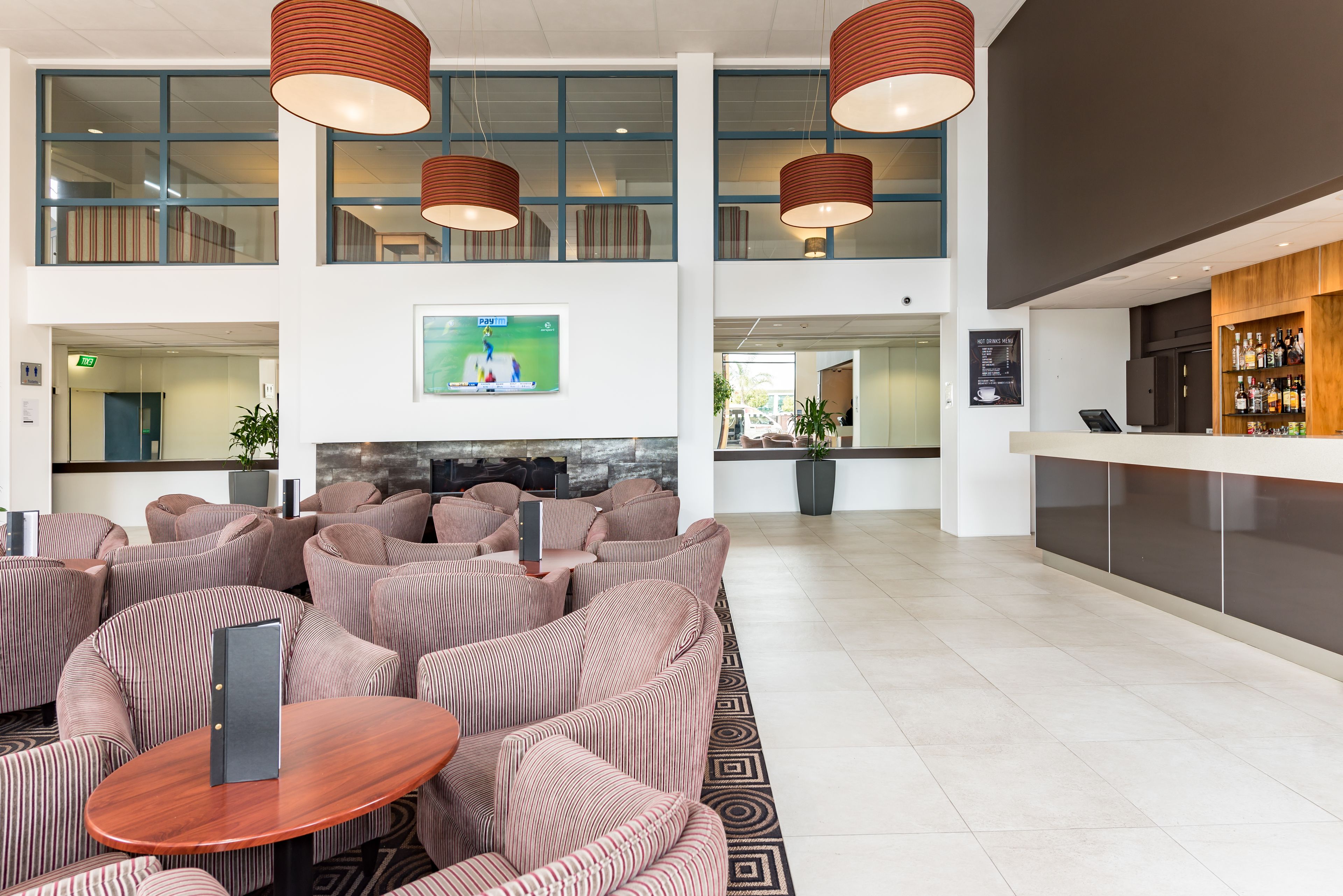 A modern lobby with striped sofas, a wooden reception desk, and a TV mounted on the wall.
