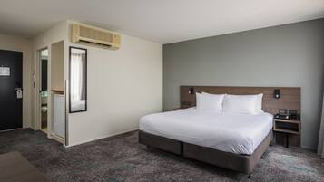 A hotel room with a large bed, a bedside table, a nightstand, a wardrobe, and an air conditioning unit.