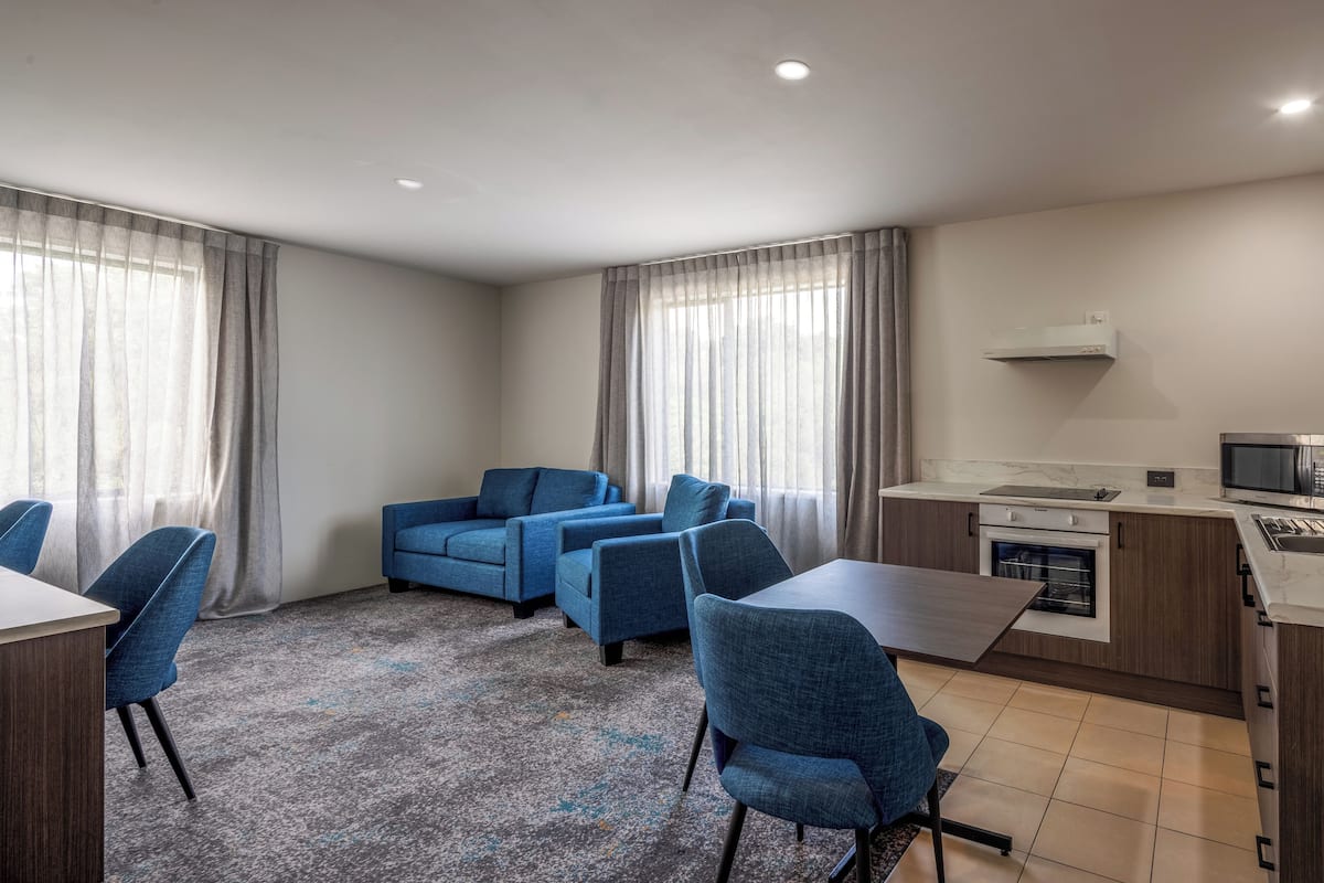 Een moderne hotelkamer met een eethoek, een kitchenette en een zithoek met blauwe sofa's.