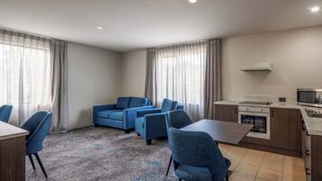 A modern hotel room with a dining area, a kitchenette, and a living area with blue sofas.