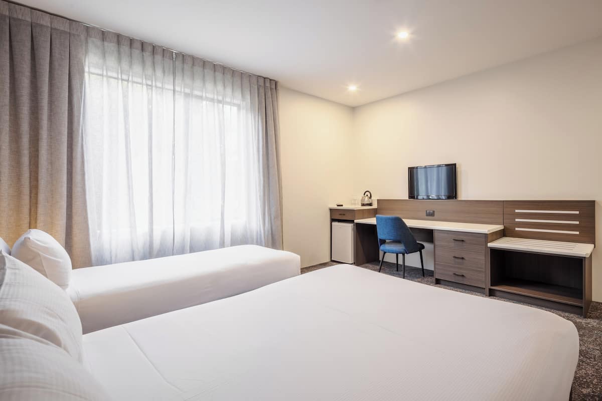 Een hotelkamer met twee bedden, een bureau, een stoel, een televisie en een raam met gordijnen.