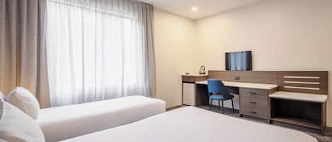 A hotel room with two beds, a desk, a chair, a television, and a window with curtains.